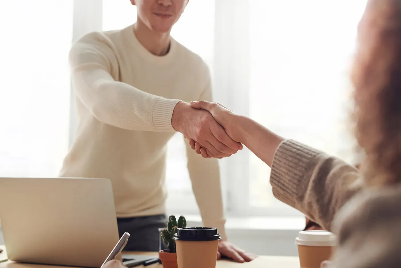 Two people shaking hands across a desk at the end of an interview